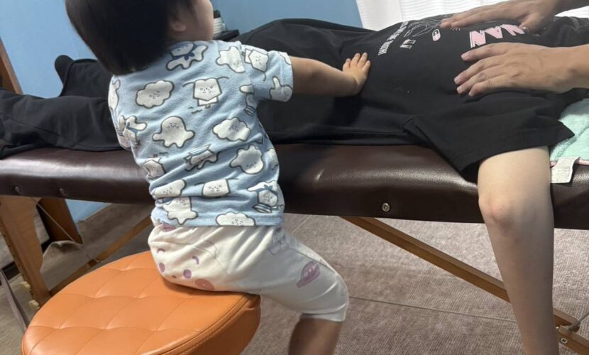 施術台の家族に手を添えて真似をする子どもと整体師の施術風景